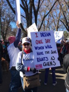 A woman holding up a sign that says " i dream one day women will have the same rights as guns ".